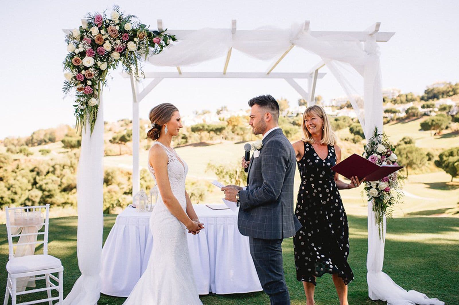 Outdoor wedding ceremony with a bride and groom exchanging vows under a floral pergola, symbolizing love and commitment, highlighting the importance of planning for the future with a prenuptial agreement.